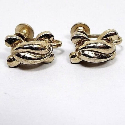 Front view of the 1940's Mid Century vintage Coro screw back earrings. The metal is slightly darkened gold tone in color from age. The middle of them has two curved teardop shapes curved against one another and then there are 4 small curved teardrop shapes curving outwards from the middle at each corner. The magnificaton shows some light scuffing from age as well.