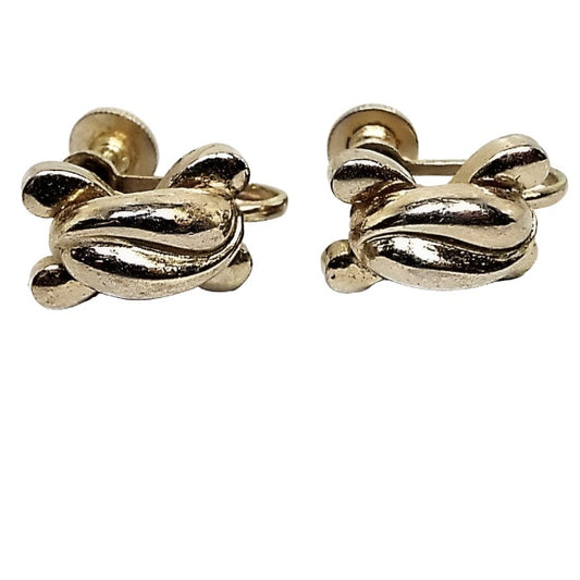 Front view of the 1940's Mid Century vintage Coro screw back earrings. The metal is slightly darkened gold tone in color from age. The middle of them has two curved teardop shapes curved against one another and then there are 4 small curved teardrop shapes curving outwards from the middle at each corner. The magnificaton shows some light scuffing from age as well.
