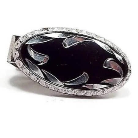 Front view of the Anson Mid Century vintage tie clip. It has a small oval shape with silver tone color metal. The inside of the oval is black with an etched design of curved teardrops flaring inwards. The outer edge of the oval is faceted with a half circle design all the way around.