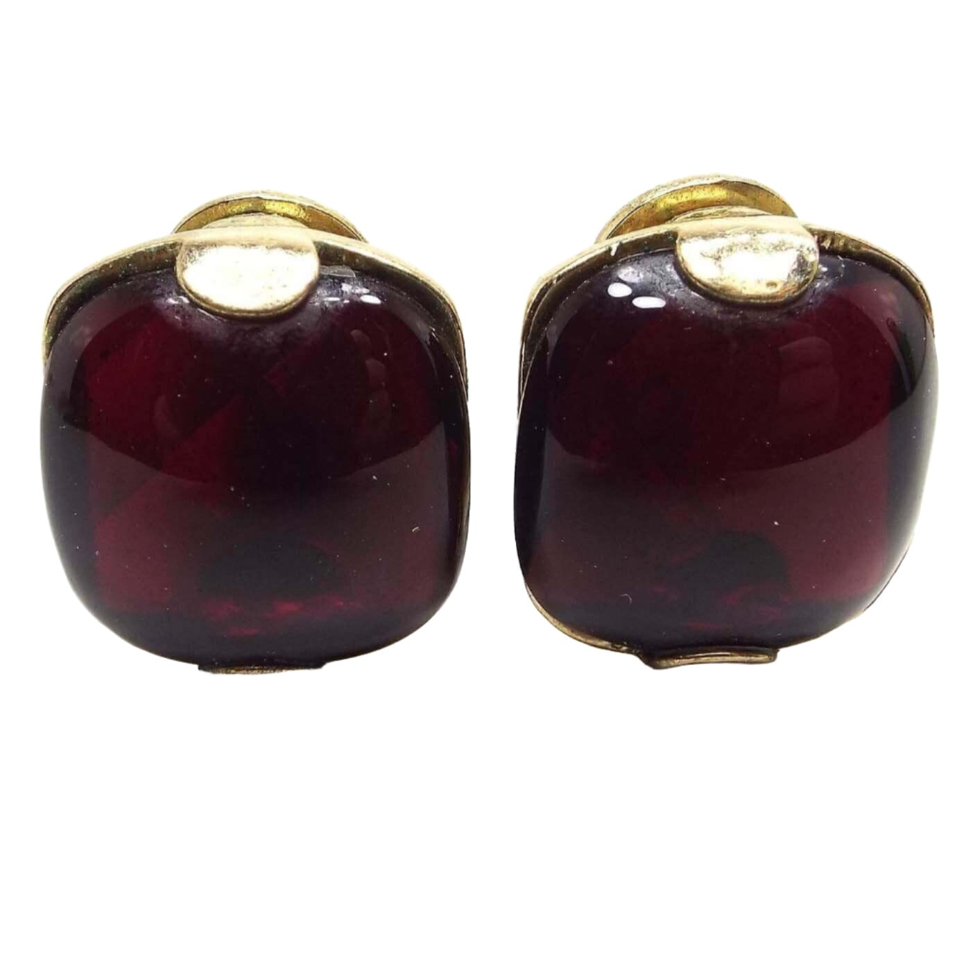 Front view of the Mid Century vintage Monet clip on earrings. The metal is gold tone in color. They are square shaped with rounded corners and have puffy lucite plastic cabs in a semi translucent dark red color. They are held on the earrings with a pront at the top and bottom that is rounded and shaped like a half moon. 