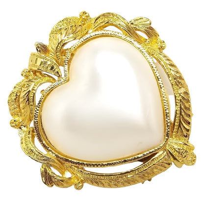 Front view of the retro vintage faux pearl scarf clip. It is shaped like a large puffy heart with a coated plastic imitation pearl heart cab in the middle. The edge has a fancy old style frame like design in gold tone color metal. 
