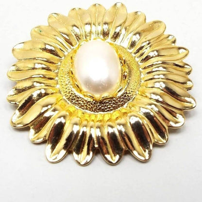 Front view of the retro vintage Jeri-Lou flower scarf clip. The metal is gold tone in color. Scarf clip is shaped like a detailed sunflower and has an oval plastic faux pearl in the middle.  