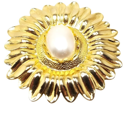 Front view of the retro vintage Jeri-Lou flower scarf clip. The metal is gold tone in color. Scarf clip is shaped like a detailed sunflower and has an oval plastic faux pearl in the middle.  