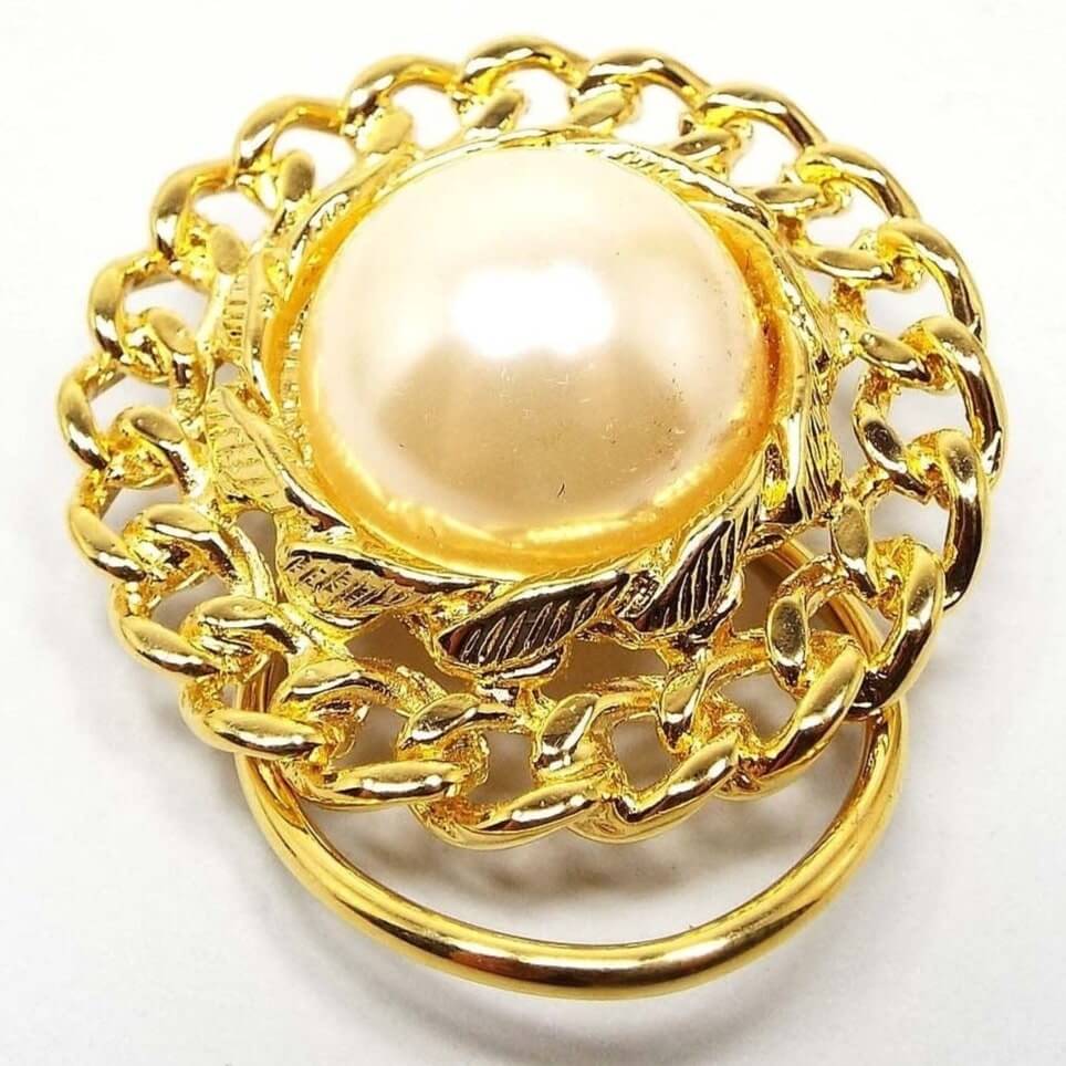 Front view of the retro vintage faux pearl scarf clip. The imitation pearl is a domed round coated plastic cab and has a curb chain like design all the way around the edge. The metal is gold tone in color.