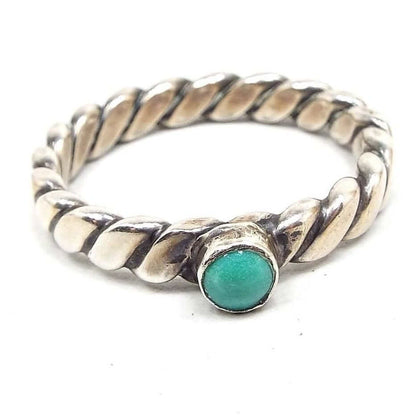 Angled front and side view of the retro vintage faux turquoise ring. The top has a small round bezel set glass imitation turquoise cab. The band has a simple flat style twist design in silver tone color metal.