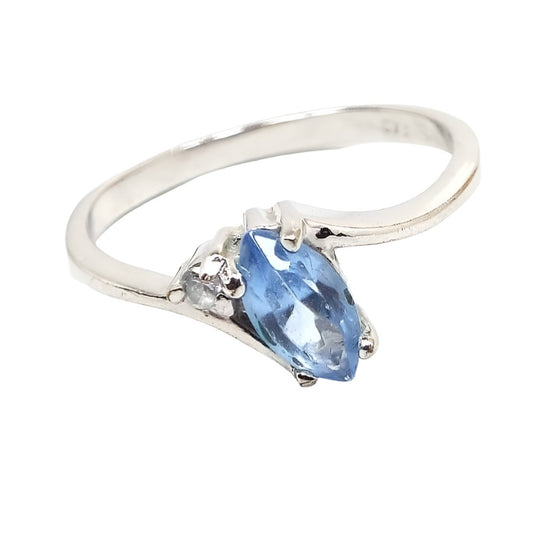 Front view of the retro vintage rhinestone ring. The metal is silver tone in color. The top has a marquis cut light blue rhinestone that looks like an oval with pinched ends. There is a small round clear rhinestones by ones corner of the blue rhinestone. The band is thinner style and has a rounded outer edge. The inside is flat and smooth.