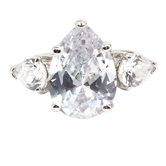 Top view of the retro vintage rhinestone cocktail ring. There is a large sized pear shaped rhinestone at the top with smaller pear shaped rhinestones on each side with their smaller ends pointing downwards. The metal band and setting is silver tone in color. All rhinestones are prong set.