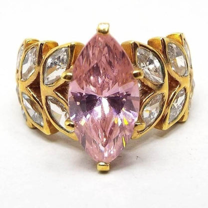 Front view of the retro vintage Edco cubic zirconia cocktail ring. The metal is gold tone in color. The middle has a larger sized marquis cut CZ stone in light pink. On the band itself on each side of the pink stone are two rows of angled marquis cut clear CZ stones giving it a leaf like design. There are six clear stones on each side. The pink stone is prong set and the rest are flush set into the band.
