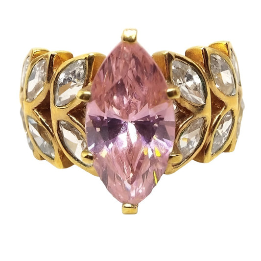 Front view of the retro vintage Edco cubic zirconia cocktail ring. The metal is gold tone in color. The middle has a larger sized marquis cut CZ stone in light pink. On the band itself on each side of the pink stone are two rows of angled marquis cut clear CZ stones giving it a leaf like design. There are six clear stones on each side. The pink stone is prong set and the rest are flush set into the band.