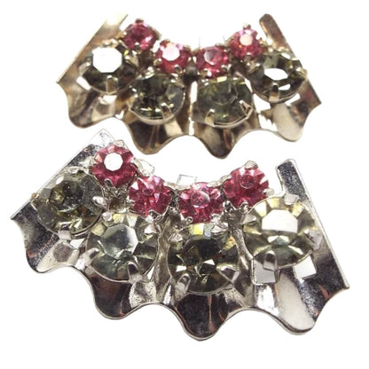 Front view of the 1950's Mid Century vintage rhinestone clip on earrings. The metal is slightly darkened silver in color. The earrings are wavy shaped curves with a row of round smoky greenish gray rhinestones on the outside and a smaller row of round pink rhinestones on the inside. All stones are prong set.