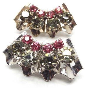 Front view of the 1950's Mid Century vintage rhinestone clip on earrings. The metal is slightly darkened silver in color. The earrings are wavy shaped curves with a row of round smoky greenish gray rhinestones on the outside and a smaller row of round pink rhinestones on the inside. All stones are prong set.