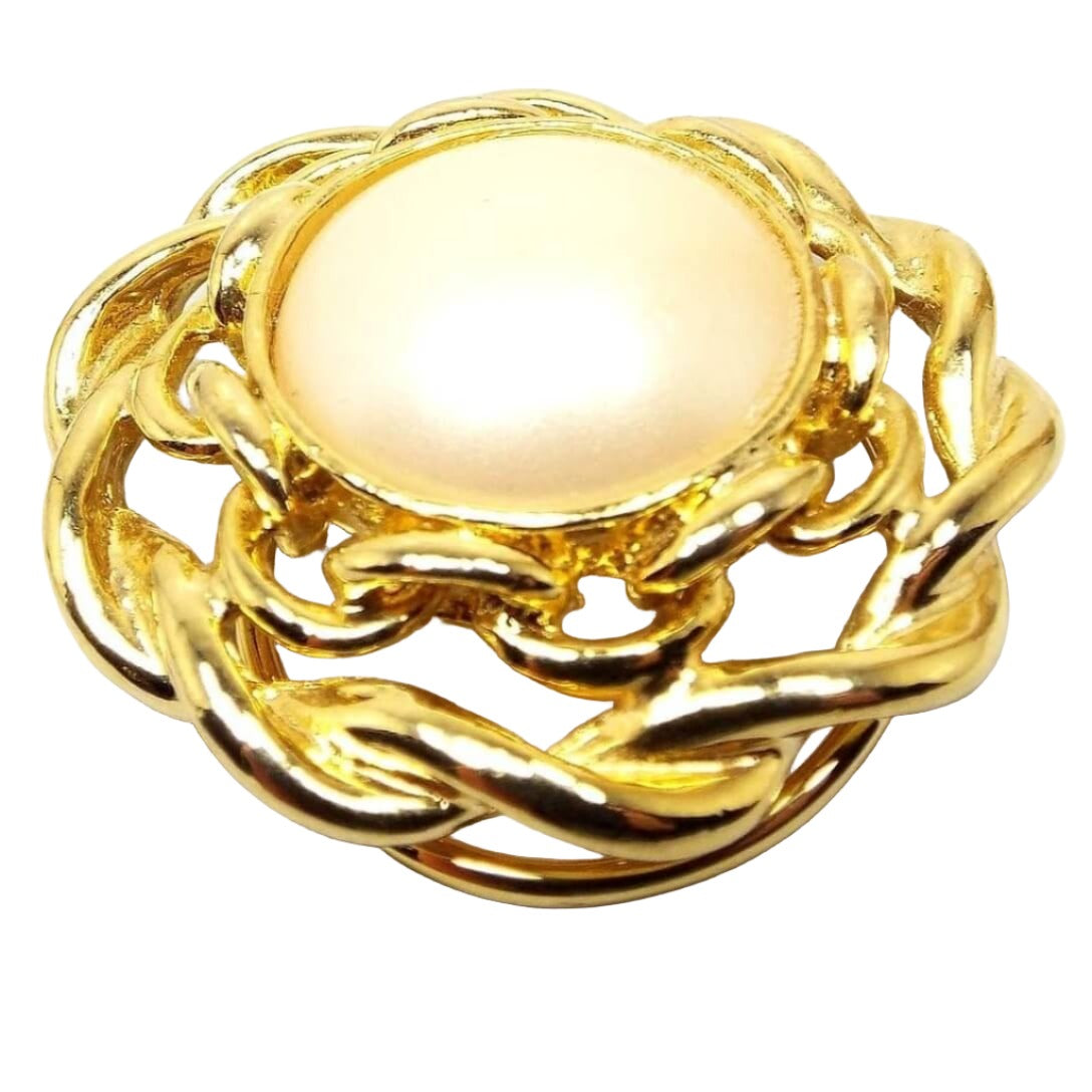 Angled front view of the retro vintage faux pearl scarf clip. There is a large off white coated plastic imitation pearl area in the middle. The gold tone color metal around the edge has a twisted woven style design with cut out areas. 