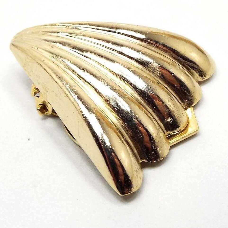 Angled front view of the retro vintage scarf clip. It has a flared corrugated fan design with shiny gold tone metal. It looks like a triangle with scalloped ends and raised curved stripes. 