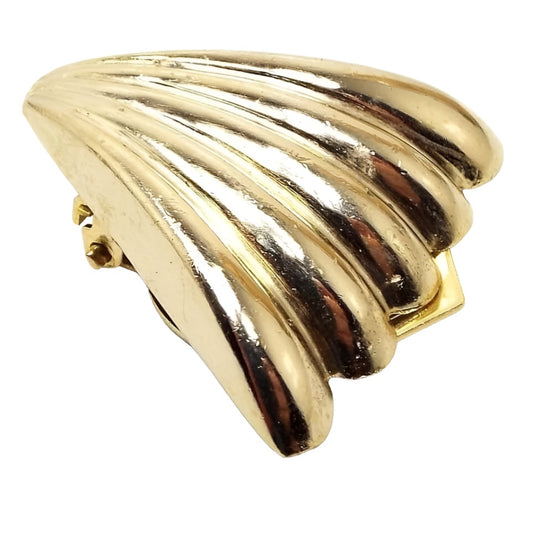 Angled front view of the retro vintage scarf clip. It has a flared corrugated fan design with shiny gold tone metal. It looks like a triangle with scalloped ends and raised curved stripes. 