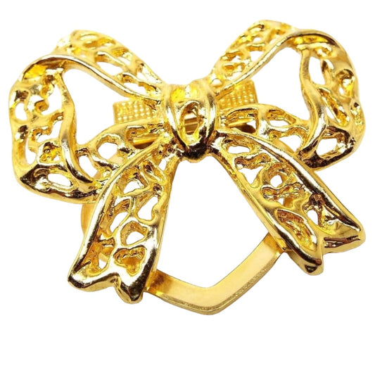 Front view of the retro vintage scarf clip. It has a filigree bow design with gold tone color metal. The back has an open flat metal hinged clasp on the back that swings open and shut.