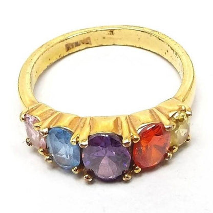 Angled front and side view of the retro vintage rainbow style rhinestone ring. The metal is gold tone in color. There are five multi color oval prong set rhinestones on top in a row that are graduating in size with the largest being in the middle. The colors are light pink, light blue, purple, orange, and light yellow. Taiwan is stamped on the inside of the band.