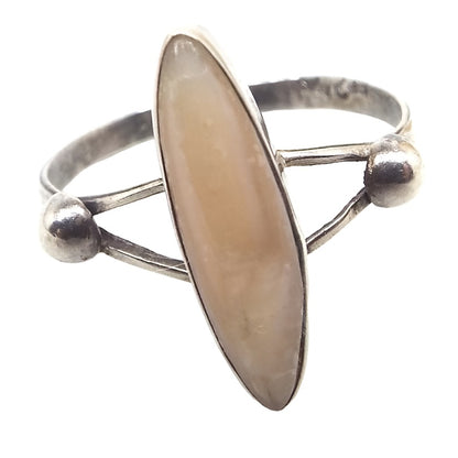 Front view of the Southwestern retro vintage Mexican sterling silver coral ring. It has a split band at the top with two domes between the split part and the rest of the band on the back. The middle has a long oval bezel setting with a coral cab that is very light peach in color. The sterling is slightly darkened. 