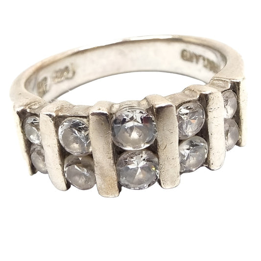 Angled front view of the retro vintage sterling silver cubic zirconia band ring. It has two rows of CZ stones curved across the top. The stones in the middle are the largest in size. All around round and channel set with sterling bars between each set of two. 925 and Thailand can be read on the inside of the band.