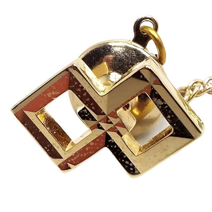 Front view of the retro vintage tie tack. There are two squares side by side in a diamond shape and the inside corners are overlapping. Each one is faceted and slopes slightly inward. The middle area of each is open. The metal is shiny gold tone in color, but there are some tiny lighter spots from age when magnified. There is a round clutch on the back that has a chain with a small bar on the end.