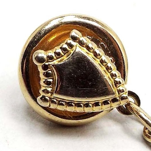 Enlarged view of the Mid Century vintage Hickok crest tie tack. The metal is gold tone in color. It is shaped like a small shield with dots around the edge.