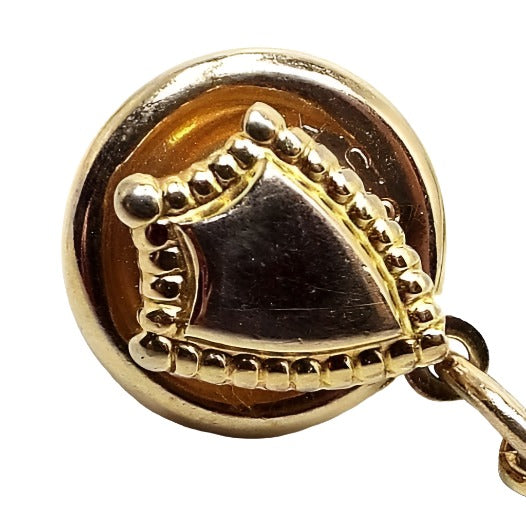 Enlarged view of the Mid Century vintage Hickok crest tie tack. The metal is gold tone in color. It is shaped like a small shield with dots around the edge.
