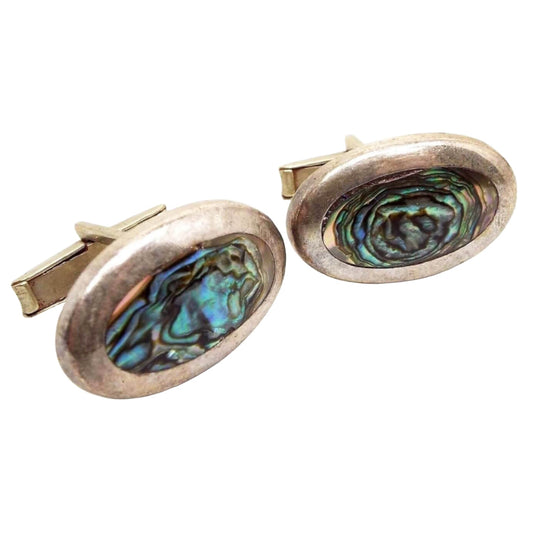 Cufflinks are silver in color. They are rounded smooth oval shaped with flat inlaid abalone shell ovals in the middle. Abalone has swirls of different colors that shimmer as you move around, but are mostly blue and green in color.