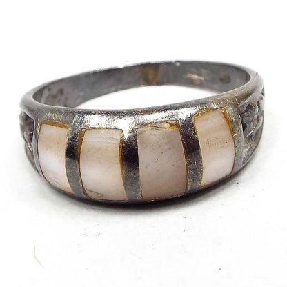 Front view of the retro vintage sterling silver mother of pearl band ring from the 1970's. It has darkened silver color from age. There are 4 vertical strips of inlaid mother of pearl shell in white and very light pink colors. Each side of the ring has a stamped textured design. 