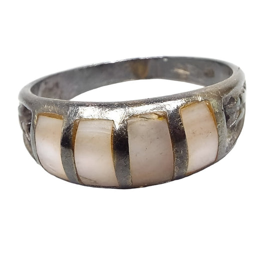 Front view of the retro vintage sterling silver mother of pearl band ring from the 1970's. It has darkened silver color from age. There are 4 vertical strips of inlaid mother of pearl shell in white and very light pink colors. Each side of the ring has a stamped textured design. 