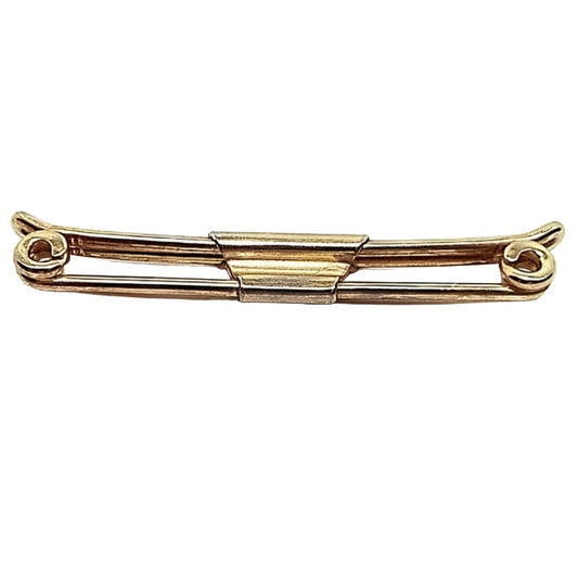 Angled top view of the 1920's Art Deco Swank vintage collar bar clip. The metal is gold tone in color. It has a basic design with rounded metal wire on front that has ends that spiral inward. The back part of the clip has ends that curve slightly outward. there is a middle trapezoid shaped piece that holds the front and back bars together.