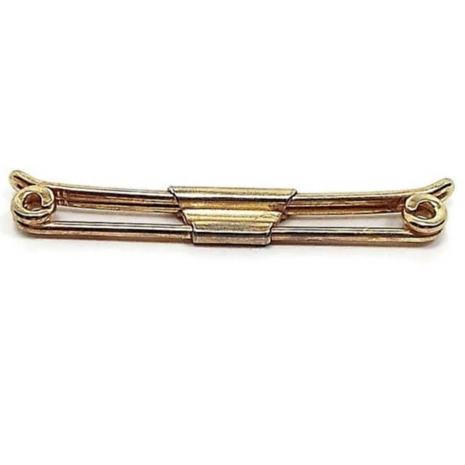 Angled top view of the 1920's Art Deco Swank vintage collar bar clip. The metal is gold tone in color. It has a basic design with rounded metal wire on front that has ends that spiral inward. The back part of the clip has ends that curve slightly outward. there is a middle trapezoid shaped piece that holds the front and back bars together.