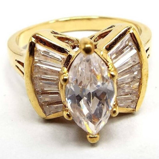 Angled front view of the 1990's retro vintage rhinestone cocktail ring. The metal is gold tone in color. The middle of the ring has a larger sized prong set marquis clear rhinestone. There is a flared out fan shape on each side of the stone that has channel set clear trapezoid shaped rhinestones in them. Each side has five trapezoid shaped stones.