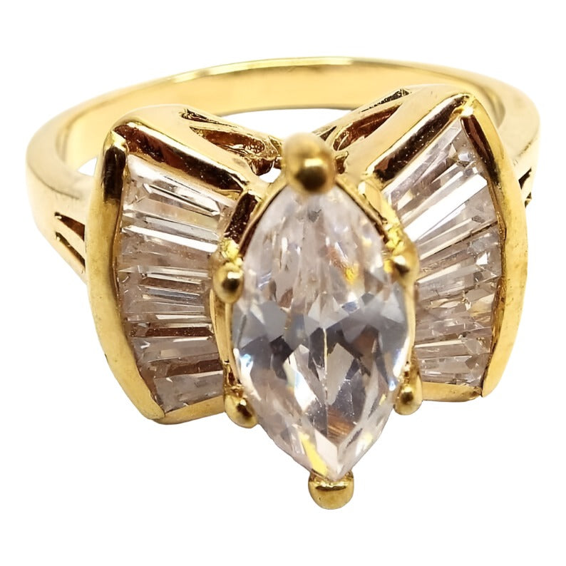 Angled front view of the 1990's retro vintage rhinestone cocktail ring. The metal is gold tone in color. The middle of the ring has a larger sized prong set marquis clear rhinestone. There is a flared out fan shape on each side of the stone that has channel set clear trapezoid shaped rhinestones in them. Each side has five trapezoid shaped stones.