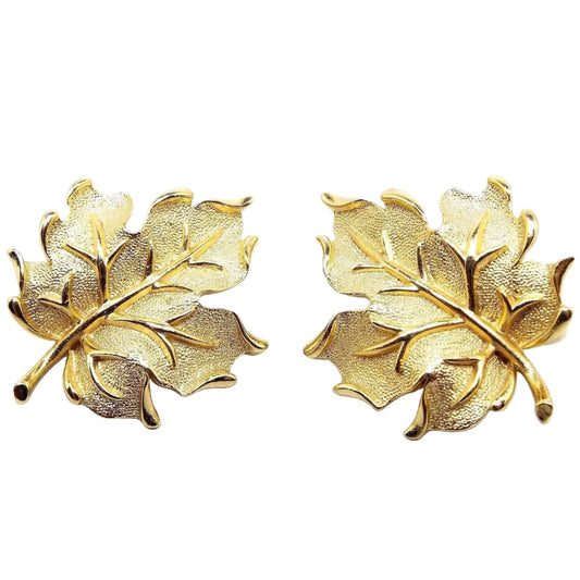 Front view of the retro vintage Crown Trifari leaf clip on earrings. The metal is gold tone in color. They are shaped like maple leaves with brushed matte textured metal on the leaves and shiny gold tone metal on the vein part and edges of the leaves. 