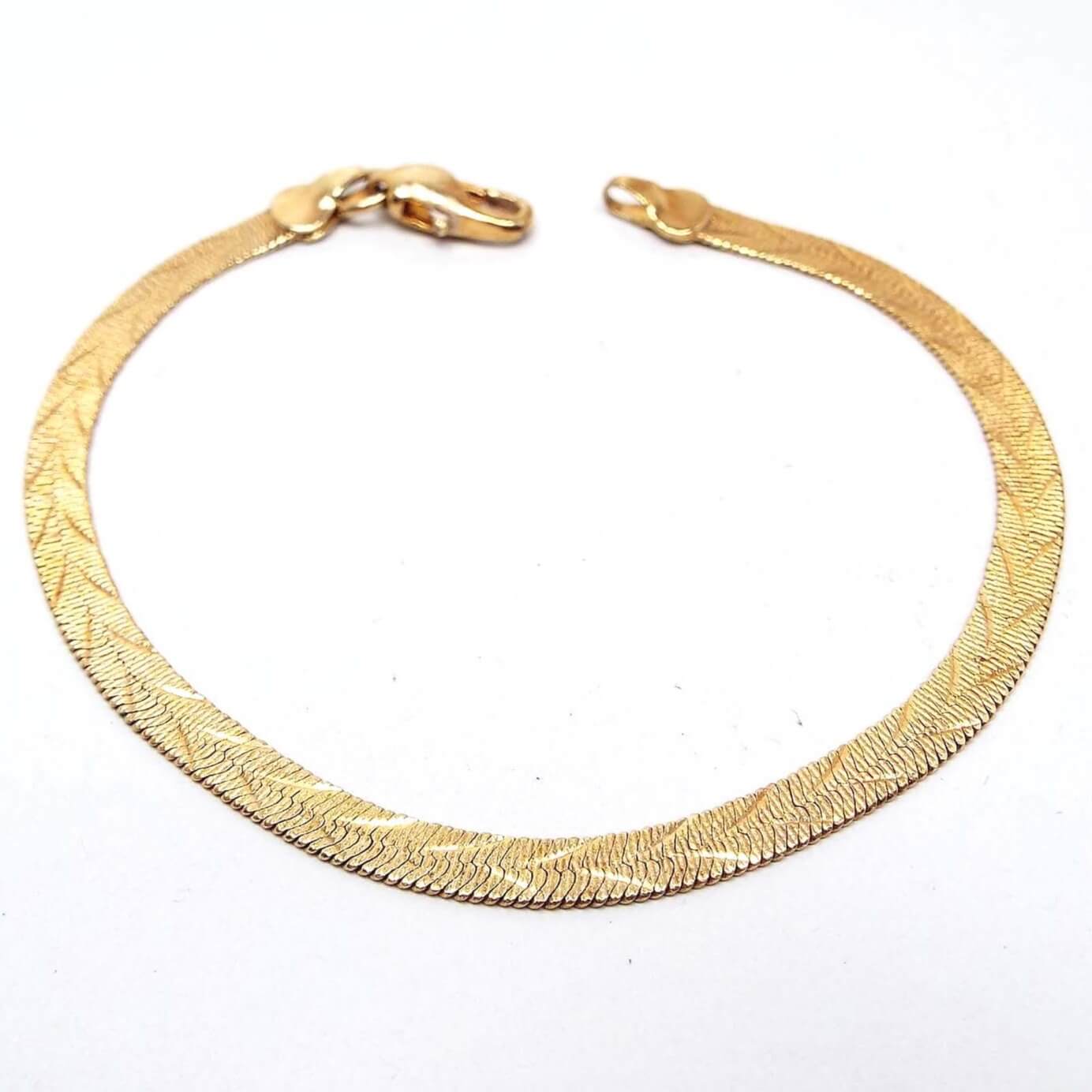 Top side view of the retro vintage reversible herringbone link chain bracelet. The metal is gold tone in color. This side has an etched V like pattern all the way down the bracelet. There is a lobster claw clasp on the end.