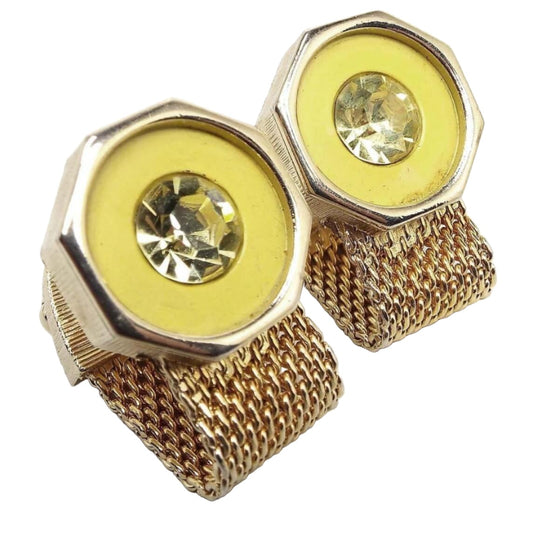Angled front and side view of the retro vintage Swank wrap around cufflinks. The metal is gold tone in color. The tops are octagon shaped with yellow glass insets and light yellow round rhinestones. The bottoms have mesh chain that is wide and curves around to the backs.