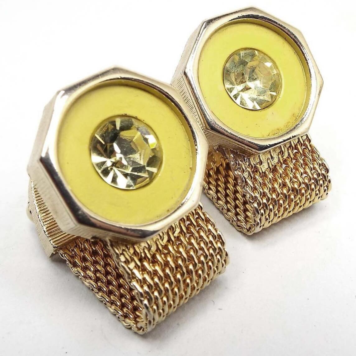 Angled front and side view of the retro vintage Swank wrap around cufflinks. The metal is gold tone in color. The tops are octagon shaped with yellow glass insets and light yellow round rhinestones. The bottoms have mesh chain that is wide and curves around to the backs.