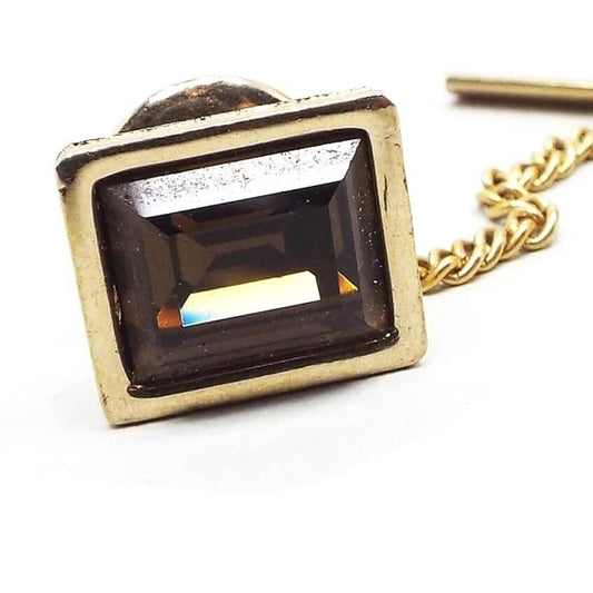 Enlarged front view of the Mid Century vintage Swank rhinestone tie clip. It's shaped like a rectangle and is gold tone in color. There is a larger sized faceted brown rectangle rhinestone in the middle. A tiny scratch in the gold tone metal can be see on the right side front of the bezel area when magnified.