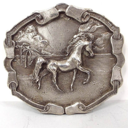 Front view of the retro vintage Bergamot Brass Works horse belt buckle. The metal buckle is pewter with varying shades of gray. The scene is a detailed raised 3D like design of a prancing Arabian style horse along the beach. There are palm trees, clouds, a sandy beach area, and very small waves in the background. The edge of the buckle is textured with small lines and has curled ribbon like areas on the top, bottom, and sides.