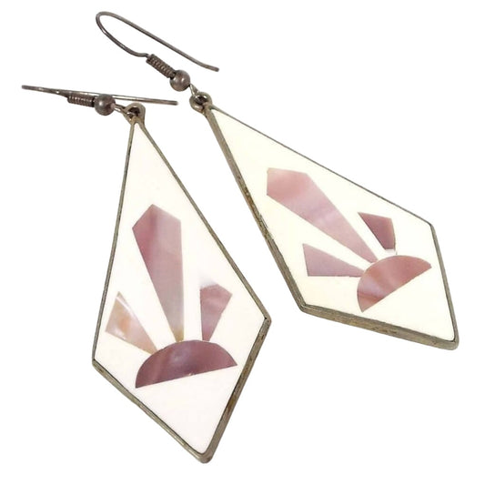Front view of the Alpaca marked earrings. Earring drops are angled teardrop shaped with white enamel. Each one has a sun ray or cactus type Southwestern style design in pearly pink color mother of pearl shell. Tops have curved fish hook style ear wires. The metal is darkened silver in color.