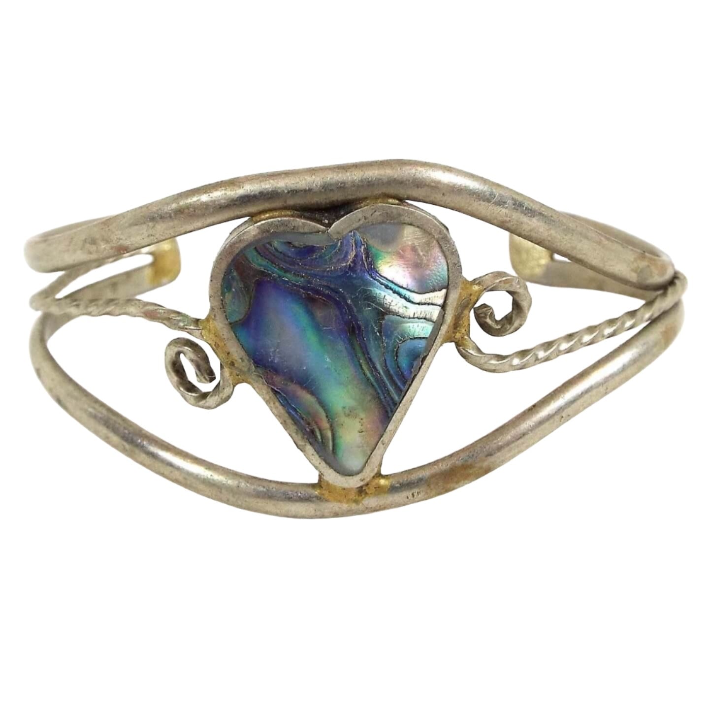 Front view of the Alpaca cuff bracelet. The bracelet is silver in color with a large heart shape in the middle. Inside the heart is inlaid abalone shell which has wavy areas of pearly multi color shell. There is a band of metal above and below the heart that curve around to form the cuff part of the bracelet, and a thinner twisted band of metal in the middle that comes off each side of the heart. 