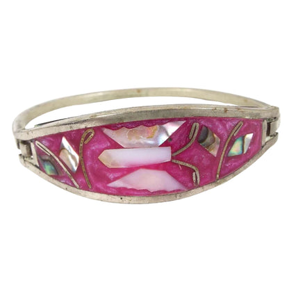 Front view of the Mexican Alpaca hinged bangle has two silver color bands of metal and a large oval area in the middle with tapered ends. The oval area has a pearly pink resin. In the middle is a butterfly with pearly mother of pearl shell wings and body. There are also abalone multi color shell leaves on each side. There is a thinner band of metal on the back side to form the rest of the bangle. One side of the bracelet has a hook type clasp that opens and closes to put it on. 