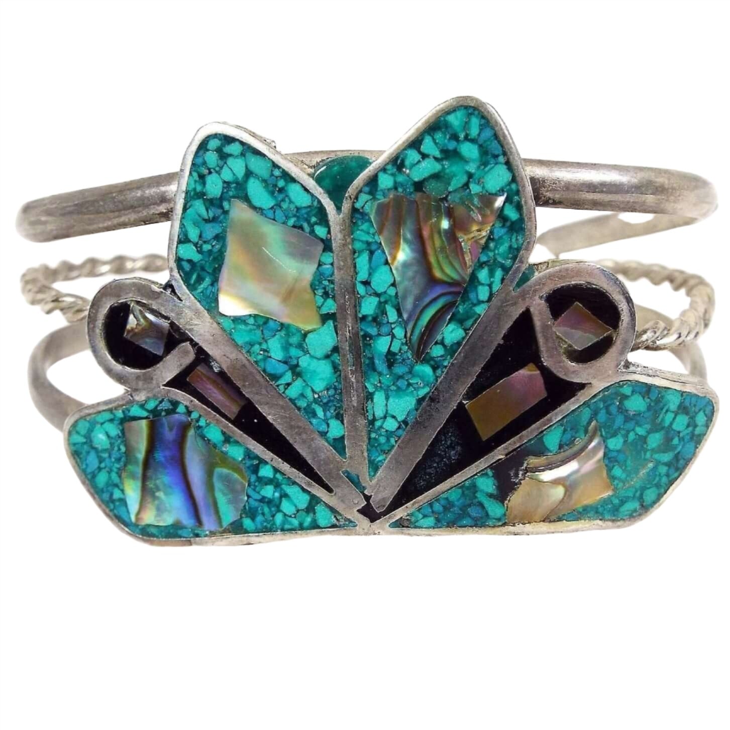 Front view of the retro vintage cuff bracelet. It is a wider silver tone bracelet with three curved bands to form the cuff. The top and bottom are rounded and the middle is thinner twisted wire. On the very top of the bracelet is a large area with angled teardops with small ends pointing inwards. Four of the larger teardrop shapes have tiny inlaid turquoise chips and a piece of inlaid abalone shell. The smaller ones have a curve of metal, black resin, and two small pieces of abalone shell. 