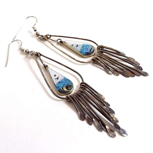  Front view of the retro vintage Mexican Alpaca earrings. Metal is darkened silver tone with hook earwires. Drops have wire tear drops with smaller sized teardrops inside them with ocean scene of sun, seagull, and water. The top part is pearly white mother of pearl shell and the bottom has tiny blue stone chips above abalone shell pieces. Hanging from the bottom are wires with flattened teardrop ends with the longest in the middle and getting shorter as it goes outward. 