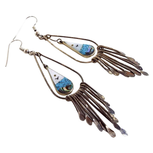  Front view of the retro vintage Mexican Alpaca earrings. Metal is darkened silver tone with hook earwires. Drops have wire tear drops with smaller sized teardrops inside them with ocean scene of sun, seagull, and water. The top part is pearly white mother of pearl shell and the bottom has tiny blue stone chips above abalone shell pieces. Hanging from the bottom are wires with flattened teardrop ends with the longest in the middle and getting shorter as it goes outward. 