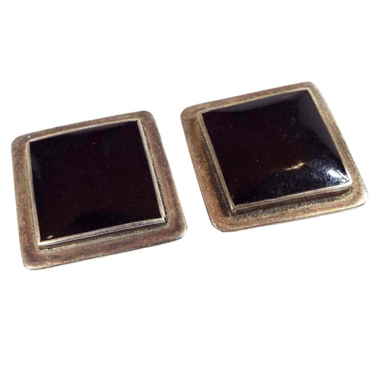 Front view of the retro vintage Mexican alpaca clip on earrings. The silver tone metal is darkened from age for a light gray color. They are square in shape but sit on the ears diagonally for a diamond like shape. The middle area has black enamel. 