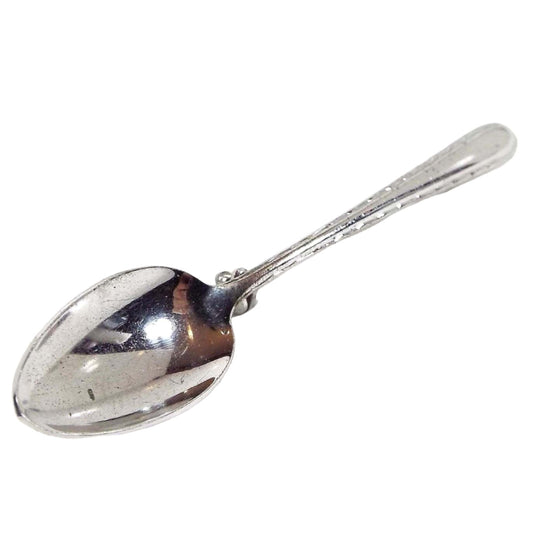 Top view of the 1940's Mid Century vintage spoon brooch pin. It is silver tone in color and shaped like a small spoon.