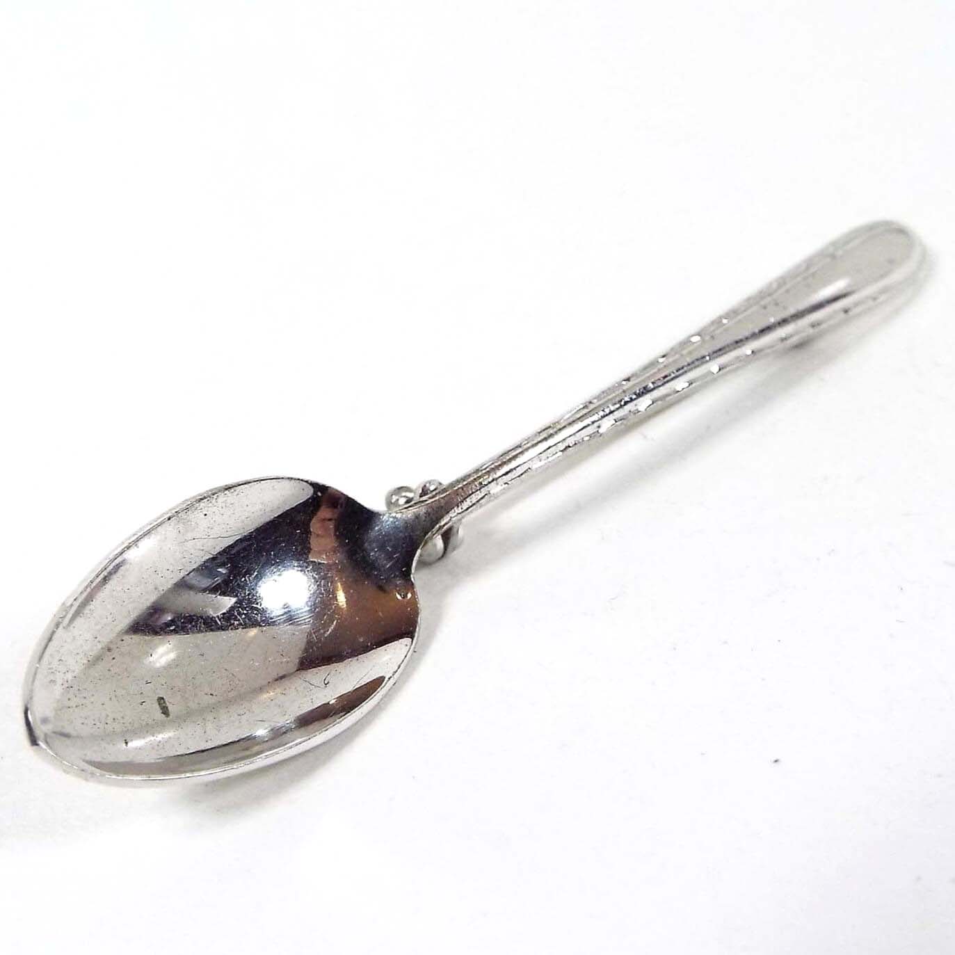 Top view of the 1940's Mid Century vintage spoon brooch pin. It is silver tone in color and shaped like a small spoon.
