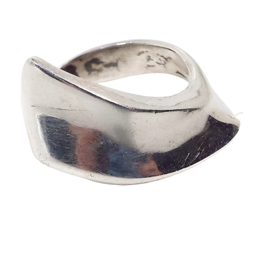 Angled front view of the retro vintage Polish 875 silver Modernist ring. The sterling is slightly darkened from age. Top of ring has a curved over design that flares at an angle on one side. There are some darkened areas on the inside of the band near where the markings are. 