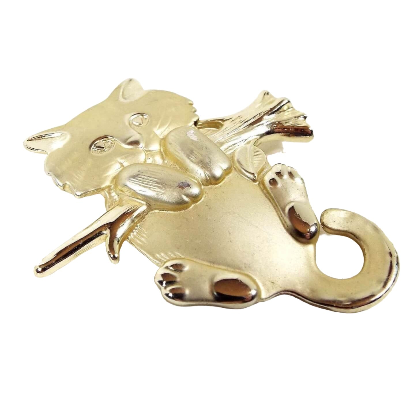 Brooch is gold in color. It has a young cat holding onto a branch facing forward. Most of the cat is matte gold in color, while the branch and toe pads on the cat are shiny gold color. Design is raised and slightly 3d in style. 