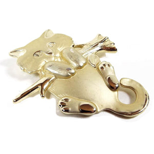 Brooch is gold in color. It has a young cat holding onto a branch facing forward. Most of the cat is matte gold in color, while the branch and toe pads on the cat are shiny gold color. Design is raised and slightly 3d in style. 